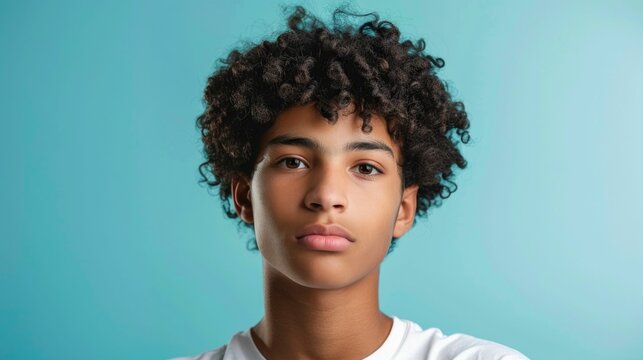 Portrait of a confident and stylish multiracial teenage boy with curly hair posing on a pastel blue studio background  The young male model has a cool serious expression that exudes a sense of modern