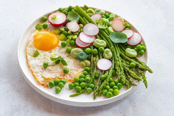 Asparagus green balanced lunch, dietary summer spring plate with asparagus, green peas, fava beans, nasturtium leaves, mint, radish, egg. Low-calorie, low-sugar lunch. New French cuisine, front view