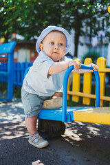 A blond-haired boy with blue eyes, an infant of 11 months, plays outside on the playground. A child...
