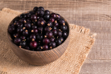 Black currant in a bowl on wooden background. Organic berries. 