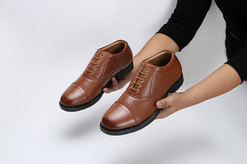 Hand holding pair of modern leather shoes on white background