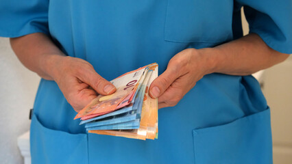 Close-up of the hands of a nurse in a turquoise uniform holding and counting money. Concept of acute shortage of medical personnel. The concept of a good salary for medical and elderly care staff.