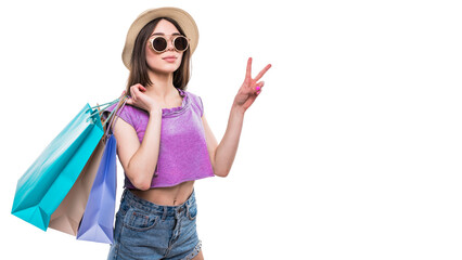 Full length portrait of a happy excited girl in bright colorful clothes holding shopping bags while standing and showing peace gesture isolated over white background