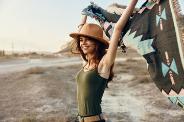 Woman in hat and tank top rejoicing in desert with arms raised holding blanket