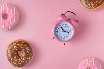 Pink alarm clock with donuts on pastel pink background. Minimal
