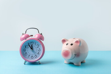 Piggy bank with alarm clock on blue table. Christmas or New Year minimal concept.