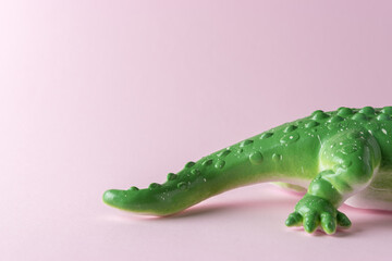 Tail of green crocodile toy on pastel pink background. Minimal art concept.