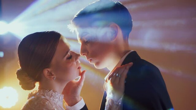 Passion and kiss of a couple in love in a nightclub. In rays of the spotlights, a woman in a chic evening dress, a man in a suit. A sensual look and touching lips of a partner. Close-up, portrait.