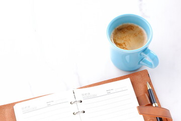 ミルクをたっぷり入れたコーヒーを飲みながら、茶色の革のシステム手帳でデスクワークをしているイメージ

