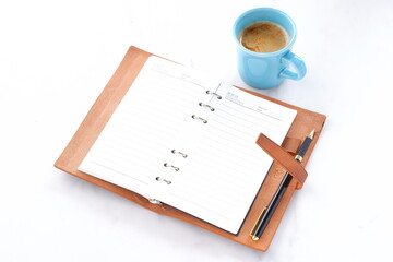 ミルクをたっぷり入れたコーヒーを飲みながら、茶色の革のシステム手帳でデスクワークをしているイメージ
