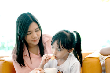 Happy family, mom and daughter are sitting in the kitchen and eating bread sticks. Cute little Asian child enjoy eating cheese bread stick.