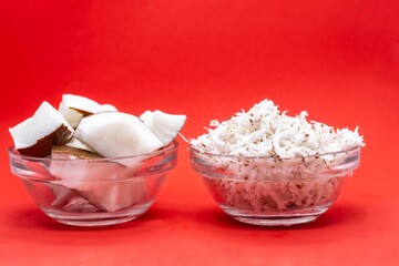 Coconut White Flesh Pieces and Grated Coconut in a Glass Bowl Isolated on Red Background with Copy Space in Horizontal Orientation