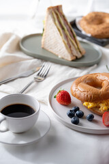 Breakfast or brunch arrangements include: Multi-layered sandwiches. Meat and Cheese Bagels placed on a tray in the background with scrambled eggs on a plate Along with strawberries and blueberries.