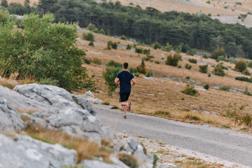 Obraz premium Determined Athlete Running Through Rugged Mountain Terrain at Sunrise.