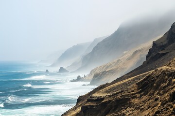 Majestic cliff coastline meets the ocean under foggy sky, creating a stunning natural panorama