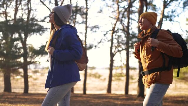 a couple of tourists are walking through the forest. forest tourism concept. happy young couple walking through the spring forest lifestyle with backpacks and sun glare. tourist