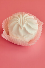 White marshmallow on bright pink background in white paper tartlet vertical shot, white dessert on pink background