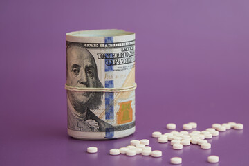 Twisted pack of hundred dollar bills and white pills, money for medicine, expensive treatment, placebo for money