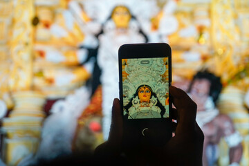 Hand holding mobile phone and taking photos of Goddess Durga idol at a pandal. Durga puja, the...