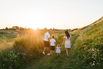 A mother, father holding hands baby daughter, son walk in mountains at sunset. Family spending time...