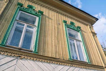 Obraz premium Windows with carved wooden frames of an old log house, sheathed in boards. An old wooden house and a blue sky. Architecture and traditions in the last century.