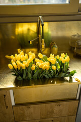 Lots of yellow tulips in a kitchen sink made in natural brass materials