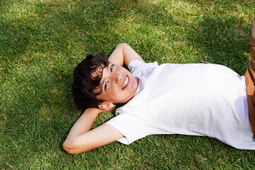 smiling pre-teen boy lying on the grass with his arms behind his head, relaxed and carefree.