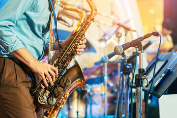 Obraz premium Musician playing saxophone on blurred background. Man with friends blow saxophone with the band for performance. Music instrument played by saxophonist player musician in festival. Selective focus.