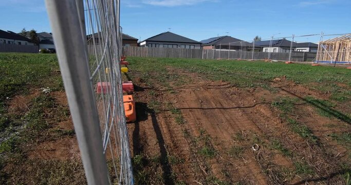 New suburban neighborhood, a plot of land designated for construction for development, fenced off by metal poles and mesh. A row of single-story houses in background. Tarneit Melbourne