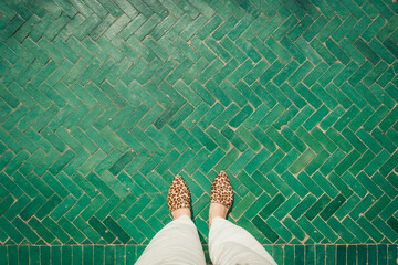 Young woman's feet selfie with leopard print shoes, bright green tiled floor, Le Jardin Secret, Morocco, modern stylish travel vacation,  summer concept background, top view personal perspective