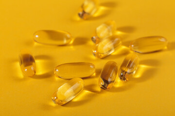 Diet, nutrition, healthy eating concept. Close up of oil filled yellow softgels capsules of food supplements on yellow background.