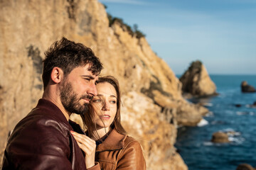 Couple enjoying a scenic view on a rocky coastline during golden hour. They are embracing and...
