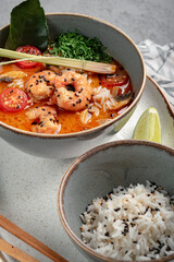 A popular dish of Asian cuisine is Tom Yam soup, cooked with shrimp, lemongrass, galangal and lime in a bowl on a gray background. Spicy and spicy Thai soup is served with boiled white rice