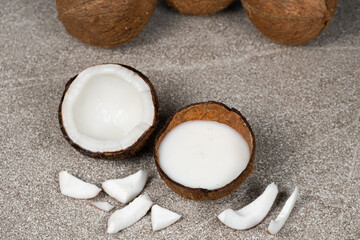 Coconut milk in coconut shell and half coconut, chopped flesh on grey background