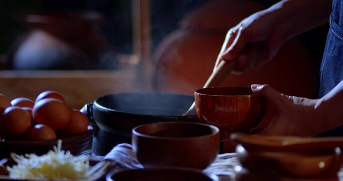 A porridge shop at night on the side of the road as the cook uses a wooden ladle to scoop porridge into a wooden bowl in a retro style. There were eggs and sliced ​​ginger placed on the table.