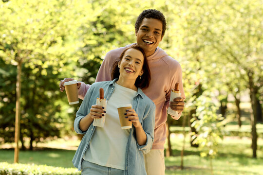 Diverse couple in vibrant attire enjoying coffee together in the park on a bright day.