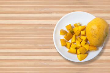 Ripe mangoes with sliced mangoes on white plate on wooden table. Healthy food concept.