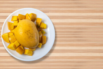 Ripe mangoes with sliced mangoes on white plate on wooden table. Healthy food concept. Close up