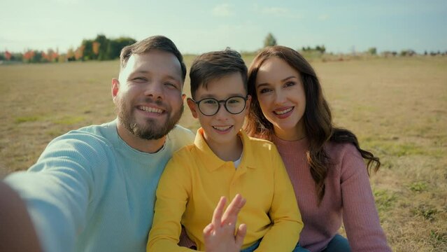 Family vacation happy Caucasian parents mom woman female dad man male little boy child son kid taking selfie record video wifi connection online call waving hands greeting looking camera nature meadow