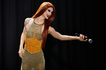 A drag queen performs on stage, microphone in hand.