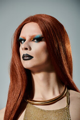 A drag diva with long red hair and dramatic makeup stares intensely at the camera.