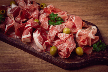 Assortment , sliced meat appetizer, prosciutto, salami and ham, with olives, on a wooden board,...