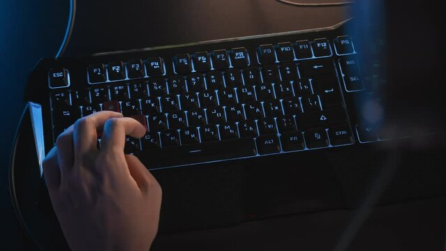 Fingers press keys on gaming RGB lightning keyboard with Cyrillic letters. Cyber sport tournament at computer club Professional E-sport championship. Gamer plays video game on PC. Multiplayer shooter