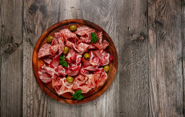 Assortment , sliced meat appetizer, prosciutto, salami and ham, with olives, on a wooden board,...