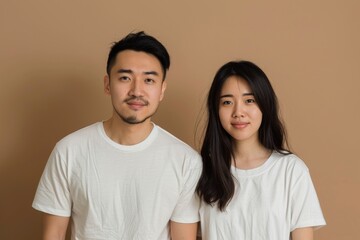 Fototapeta premium Portrait of a content asian couple in their 20s dressed in a casual t-shirt isolated on soft brown background