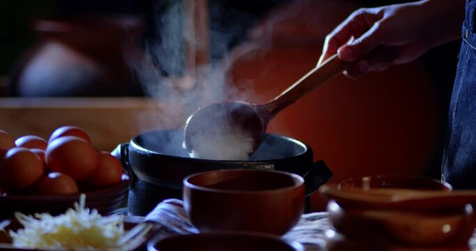 A porridge shop at night on the side of the road as the cook uses a wooden ladle to scoop porridge into a wooden bowl in a retro style. There were eggs and sliced ​​ginger placed on the table.