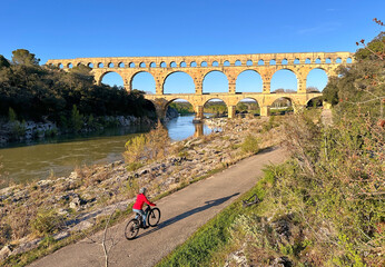senior woman mountainbiking with her e bike below the famous roman aqueduct of Pont du Gard near...