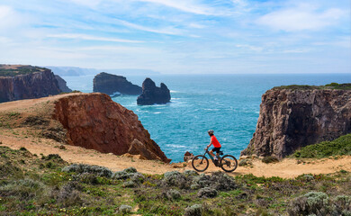 happy active senior woman cycling on the the rocky cliffs of the Vicentina coast of  Algarve,...