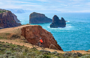 happy active senior woman cycling on the the rocky cliffs of the Vicentina coast of  Algarve,...