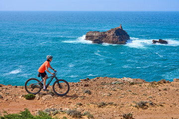 Fototapeta premium happy active senior woman cycling on the the rocky cliffs of the Vicentina coast of Algarve, Portugal near Sagres and Vila do Bispo 